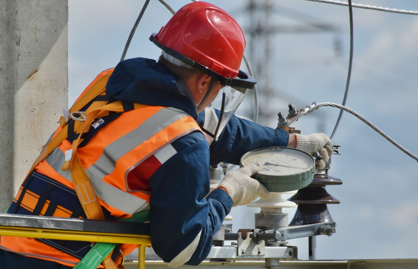 Technician in safety vest adjusts electrical equipment outdoors.