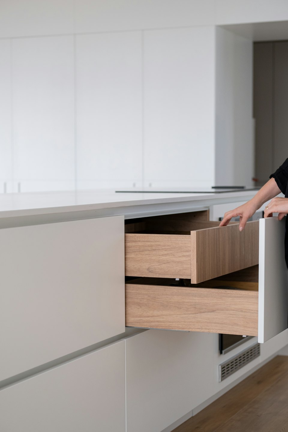Hand opening a light wood drawer in a modern kitchen.
