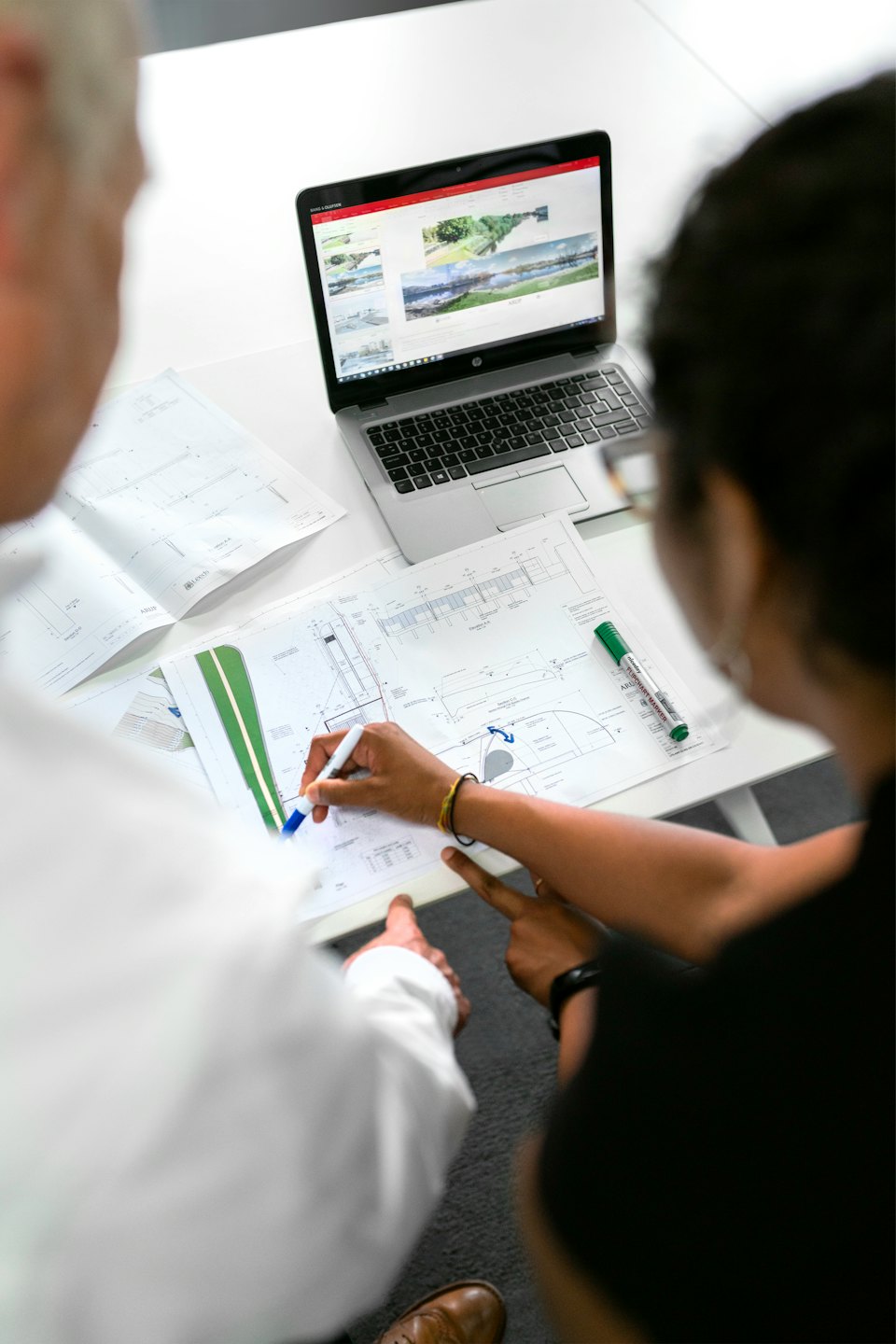 Two colleagues review architectural plans on a desk.
